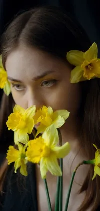 This beautiful live wallpaper features a woman holding a bunch of yellow flowers against her face in a dramatic low-key studio lighting