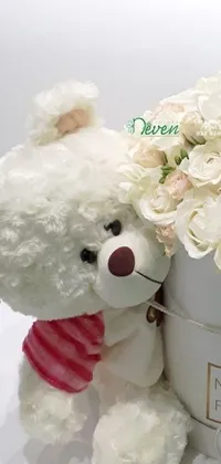 This phone live wallpaper features a cute white teddy bear sitting alongside a white box filled with charming flowers