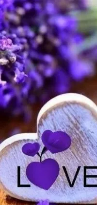 This phone live wallpaper showcases a wooden heart inscribed with the word "love", complemented by tender violet flowers