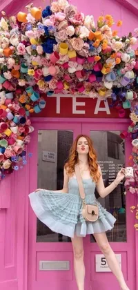 This live phone wallpaper depicts a woman posing in front of a bright pink tea shop surrounded by a variety of colorful flowers