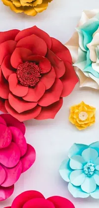 This lively phone wallpaper features a vibrant close-up of fuchsia, vermillion, and cyan paper flowers in varying sizes on a wooden surface