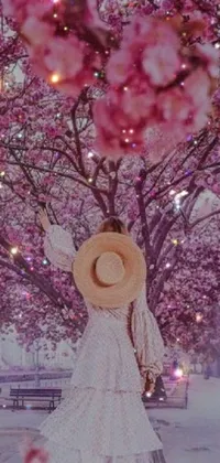 Introducing a mesmerizing phone live wallpaper featuring a woman standing under a beautiful tree adorned with pink flowers