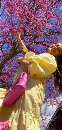 This phone live wallpaper showcases a vibrant woman in a yellow dress, holding a pink frisbee against a cherry blossom tree