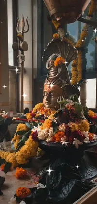 Elevate your phone screen with a beautiful live wallpaper featuring a divine statue of Samikshavad sitting on a flower-adorned table