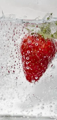 This phone live wallpaper features a photo-realistic image of a red strawberry in a glass of water