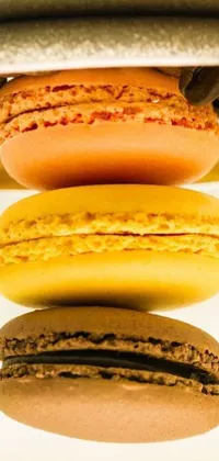This mobile wallpaper displays a close-up photograph of a stack of mouthwatering macarons, composed by using a warm ocher color scheme with a glazed, shiny finish