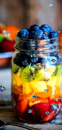 This colorful mobile live wallpaper features a glass jar filled with fresh fruits in a rainbow of blueberry, orange, and teal shades sitting on a rustic wooden table