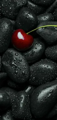 This mobile wallpaper showcases a stunning close-up view of a bright red cherry surrounded by black rocks