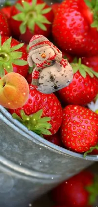 This lively and colorful phone wallpaper captures a bucket filled with delectable red berries sitting on a rustic wooden surface