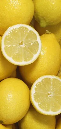 This lively phone wallpaper features a pile of plump lemons with one sliced in half, showcasing bright yellow citrus droplets and seeded flesh