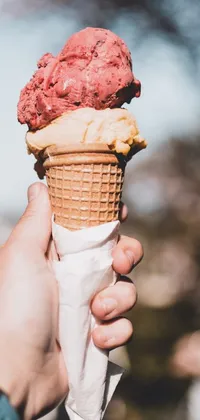 Bring summer vibes to your phone screen with this live wallpaper! Featuring a mouth-watering closeup shot of an ice cream cone in hand, this wallpaper's pink hues perfectly complement the lush green foliage in the background