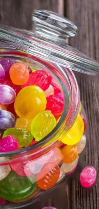 This live wallpaper features a glass jar full of colorful jelly beans on a wooden table, with spilled candy scattered around it