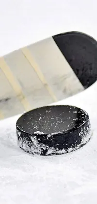Upgrade your phone's background with this striking live wallpaper featuring a vivid image of a hockey stick and puck settled on snow-covered ground