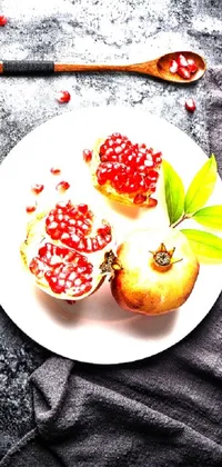 This phone live wallpaper features a still life of a white plate topped with pomegranate seeds and a wooden spoon, captured by a talented photographer