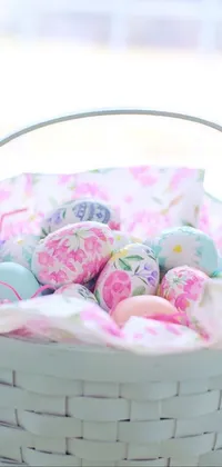 This phone live wallpaper features a beautifully decorated basket filled with vibrant pastel Easter eggs sitting on top of a wooden table