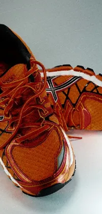 This live wallpaper features a pair of orange running shoes positioned on a white surface, portrayed in a photorealistic manner