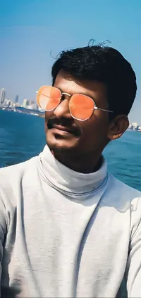 Get lost in the serenity of this phone live wallpaper featuring a man wearing orange shades, gazing out at the sea behind the city