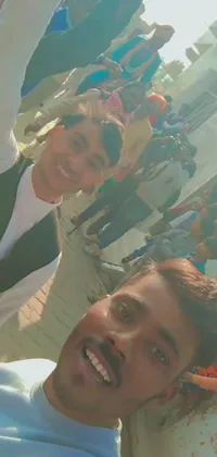 This phone live wallpaper captures a couple taking a selfie in front of a crowd, with two young men in jodhpuri suits cheering in the background