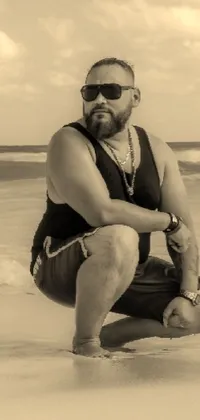 This live wallpaper depicts a bearded man in a classic black and white photo, kneeling on a sandy beach next to the ocean