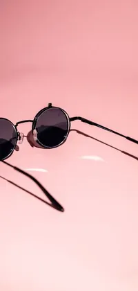 Looking for a unique and trendy live wallpaper for your phone? This design features stylish sunglasses on a pink surface, complete with a modern and sophisticated black color scheme that will appeal to any fashion-forward individual