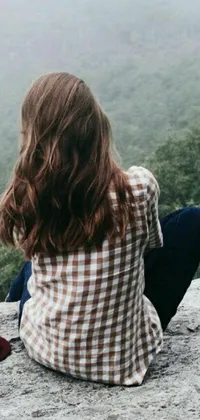 This live phone wallpaper showcases a woman in a countryside setting, sitting atop a large rock
