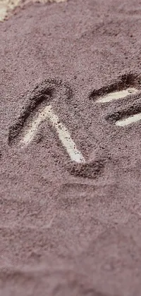This phone live wallpaper features a beautiful heart drawn on a mauve sand beach with sand chalk art, graffiti designs, and math equations in the background