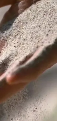 This stunning phone live wallpaper captures the beauty of soft sand in a person's hands