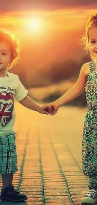 Looking for a sweet and charming live wallpaper to add to your phone? Look no further than this beautiful image featuring two adorable children holding hands as the sun sets in the background