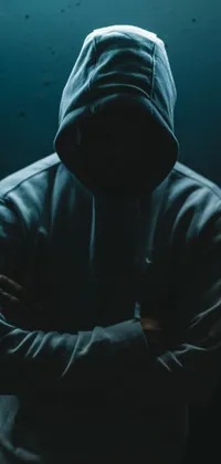 Get a live wallpaper for your phone featuring an enigmatic scene with a man in a hoodie standing and crossing his arms