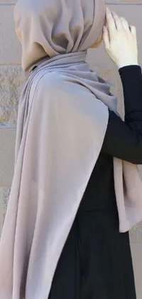 This live wallpaper features a hijab-wearing woman standing in front of a textured brick wall in a sandy desert