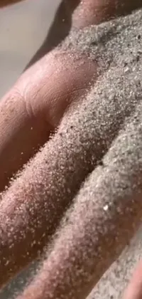This stunning phone live wallpaper features a captivating close-up of a hand holding sand