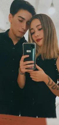 This live wallpaper depicts a stylish scene of a man and woman taking a selfie together in front of a mirror