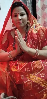 This phone live wallpaper depicts a woman wearing a beautiful red sari, sitting gracefully on the floor in a festive attire
