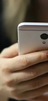 This mobile live wallpaper features a close-up of a hand holding a cell phone displaying an animated background or a live feed of the device's notifications