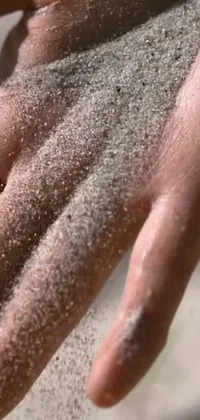 This live phone wallpaper shows a detailed view of a hand filled with sand