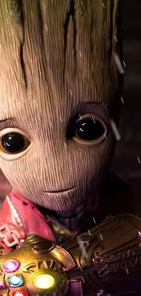 This stunning live wallpaper for phones features a close-up of a toy baby grooter dressed in a Groot costume, holding the Infinity Gauntlet