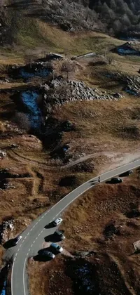 This phone live wallpaper showcases a group of cars cruising down a winding road surrounded by a scenic natural environment
