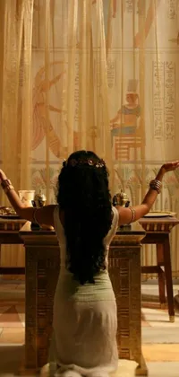 This phone live wallpaper features an Egyptian woman sitting at a table, with a vase and a bowl in front of her