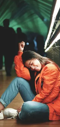 This live phone wallpaper showcases a beautiful woman in an orange coat seated on the floor in a tunnel