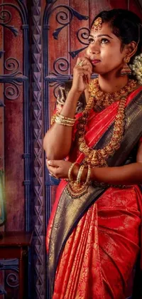 This beautiful phone live wallpaper showcases a stunning Indian woman dressed in a bright red sari standing in front of a decorated door