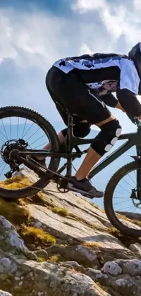 This phone live wallpaper features an action-packed and hyper-realistic image of a mountain biker traversing down a steep, rocky slope