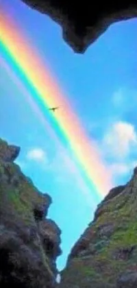 This live mobile wallpaper depicts a heart-shaped hole with a vibrant rainbow in the sky, set against a backdrop of a mysterious cave