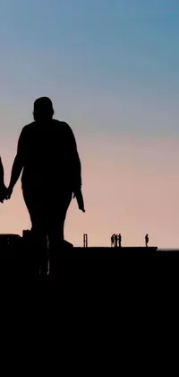 This live phone wallpaper shows the silhouette of a couple walking through a field during sunset