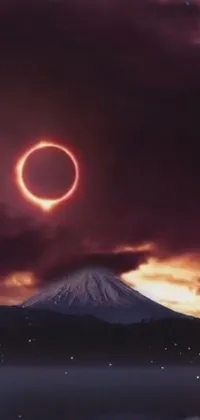 This live phone wallpaper by Tadashi Nakayama showcases a stunning, realistic image of a fiery ring in the sky during an eclipse, set against a majestic mountain