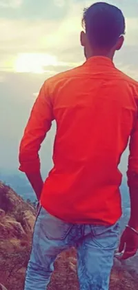 This phone live wallpaper depicts a man admiring a stunning mountain vista, dressed in bold orange clothing