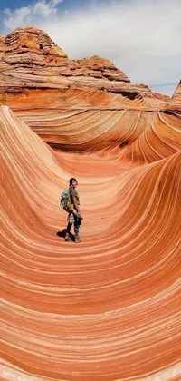 This live phone wallpaper showcases a striking scene of a man walking amid wavy sandstone formations in the desert