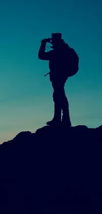 Looking for a stunning phone live wallpaper? Check out this romanticism-inspired image featuring a man standing on a mountain holding a camera