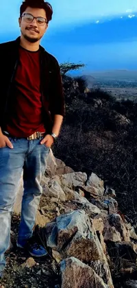 This live wallpaper depicts a man standing on top of a rocky hill, dressed in jeans