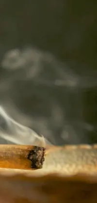 This phone live wallpaper showcases a close-up of a lit cigarette emanating smoke