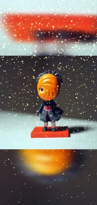 This phone live wallpaper features a cute figurine sitting on an orange with a stunning tilt shift photo background